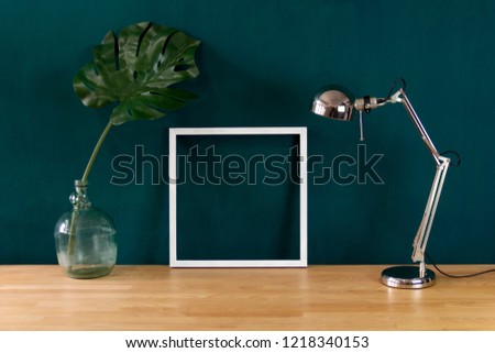 Work desk decorated with white photo frame and tropical monstera leaf 