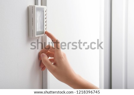 Woman adjusting thermostat on white wall, closeup. Heating system Royalty-Free Stock Photo #1218396745