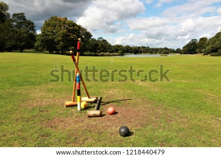Field trees and cloudy blue sky featuring a croquet set and balls unattended as if left behind after a game Royalty-Free Stock Photo #1218440479