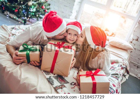 Beautiful family in Christmas interior.Happy parents kissing daughter and giving xmas present.
