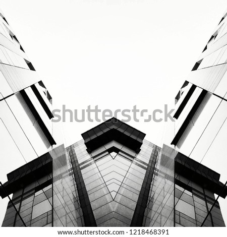 Black and white mirror shot of a glass building. The shot was taken whilst looking up at the building. The building is mainly made of glass and black, grey and white lines giving a V sign or wing view
