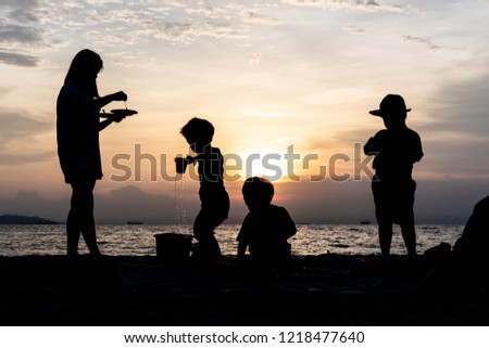 The silhouette of kids and mother are playing and eating at the beach in evening.