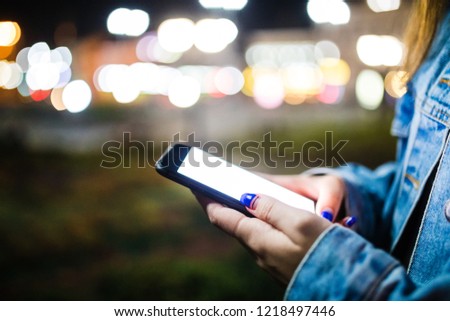 Close up female hands using mobile smartphone in illuminated color light bokeh on street night background