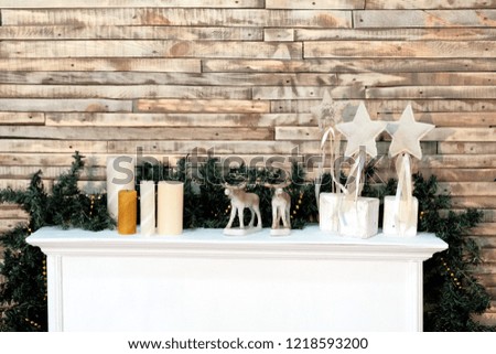 Christmas background decor in the room. Creative for in the style of the new year. White shelf with candles, stars and deer figures. Wooden wall Copy space, a place for different inscriptions.