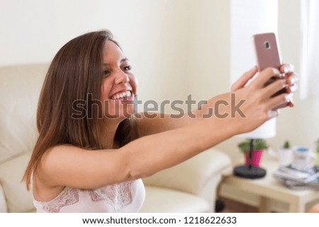 European brunette girl, making a selfie with her mobile arms raised and happy, smiling very happy and nice in the living room of her house