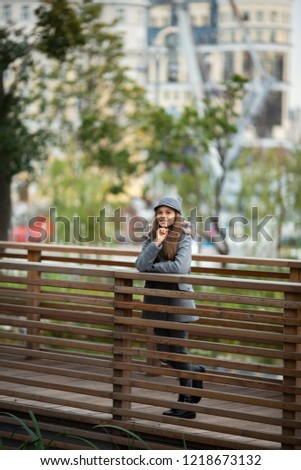 Photo of girl in gray hat and coat on wooden bridge in city