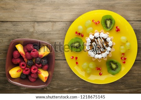 dessert of cake and fruit (grapes, kiwi, pomegranate) on a wooden background. dessert on a plate top view