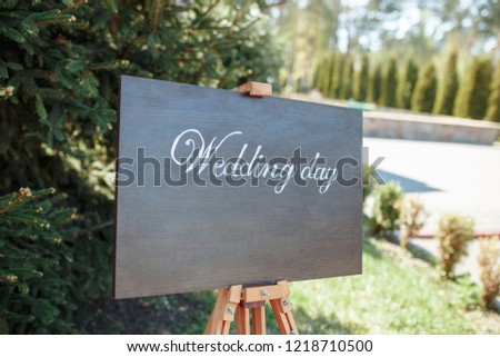 The close-up photo of the wooden plaque with the signs Welcome to the wedding standing in the street on a green banquet background. wedding decor