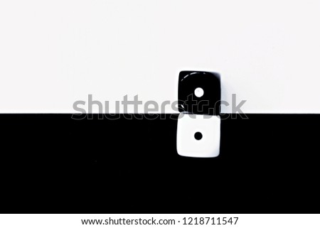 A white dice on a black background and a black dice with a white background lie side by side - concept with contrasts and dice