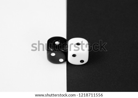 A white dice on a black background and a black dice with a white background lie side by side - concept with contrasts and dice