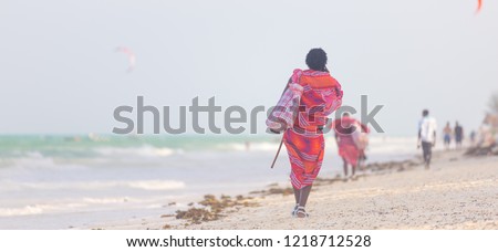 Rear view of traditonaly dressed maasai man walking the sand and selling hand made jewelry on picture perfect tropical Paje beach, Zanzibar, Tanzania, East Africa.