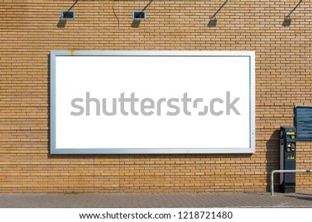 Blank white billboard for advertisement mounted on the brick wall near car parking.
