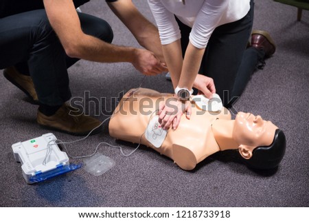 CPR training medical procedure workshop. Demonstrating chest compressions and use of AED automatic defibrillator on CPR doll. Royalty-Free Stock Photo #1218733918