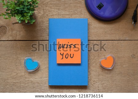 Blue book with message "miss you" on wooden desk background; flat layout.