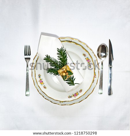 Christmas dinner set: porcelain plates, silver cutery and white napking lying via diagonal line with christmas decoration. Flatlay. Copy space.