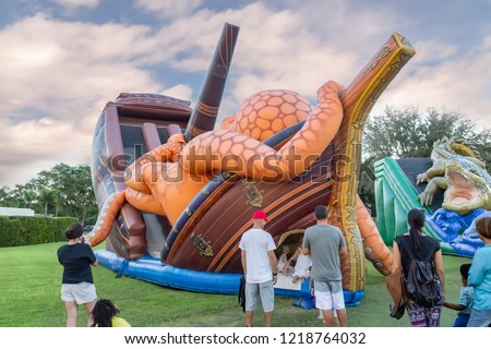 Festival filled with a much-themed bounce house for kids to enjoy. Parents and children gather in front of the large community bounce house shaped like an octopus on top of an old ship.