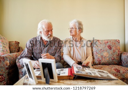Senior european couple of pensioners sitting in cozy living room looking at photos from their wedding day and first child birth and recollecting happy moments of life. Happy family, old age concept