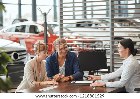 Agreement or contract concept. Confident young female sales manager offering car purchase contract to young couple at car dealership office.