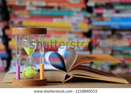 Close-up of hourglass on table in library The book opens at the book page, rolls into a heart-shaped background selective focus and shallow depth of field
