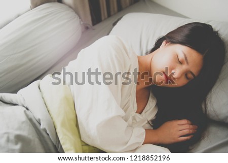 Image of a woman sleeping in a bed with blanket covering herself. Bedroom.