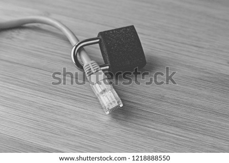 A cyber security concept image consisting of an Ethernet cable, padlock and a wooden background.  Black and white image. 