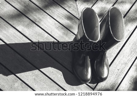 A black and white image of two black gumboots on a wooden deck.