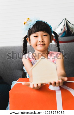 Portrait of a cute girl holding house model over gift box and looking at camera.