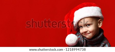 Funny funny little boy in a Santa Claus hat on a red background, banner size, free space for text