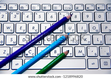 blue green and purple pencils lie on a silver computer keyboard
