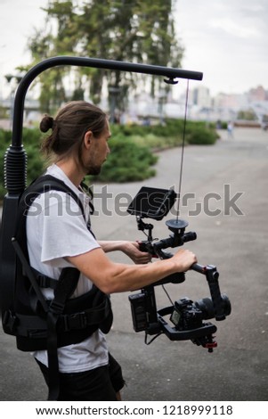 Professional videographer holding camera on 3-axis gimbal which mounted on easy rig. Videographer using steadicam. Pro equipment helps to make high quality video without shaking.