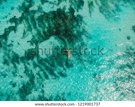 Turquoise ocean water and relaxed swimming woman, aerial drone shot. Top view