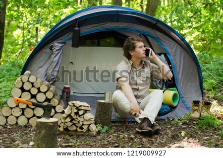 Backpacker uses a smartphone outdoors. Campground in nature.