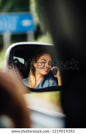 Attractive young woman in the car talking on the radio to the other people. Travelling all arounf the world. Warm autumn weather. Photo in the mirror.