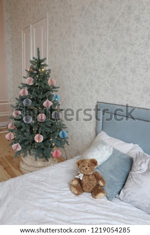 Christmas tree with pink and gray paper toys in the bedroom with a soft blue bed and a toy bear on it in the luxury apartments