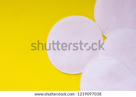 White cotton pads for removing makeup are on yellow uniform background view from above with clear area of half of photo for labels or headers. Hygienic products for cleaning face, skin hygiene 