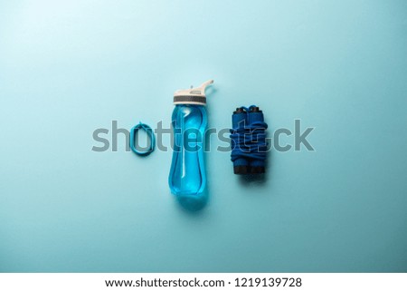flat lay with fitness tracker, sport bottle and jump rope placed in row isolated on blue, minimalistic concept 
