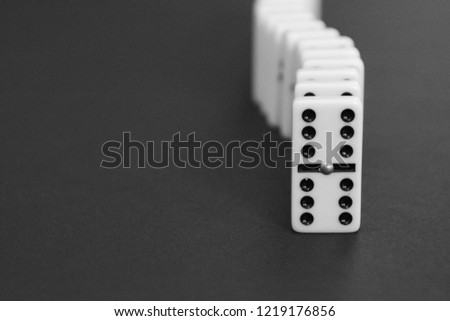 White dominoes stand in a row against a dark background as a symbol of a coherent task or the subsequent reactions of various ideas and tasks