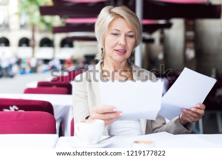 Mature woman is lunching and reading documents in cafe.