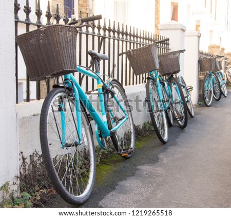 A row of matching rental bicycles with baskets are chained up to a fence outside a student house in cambridge