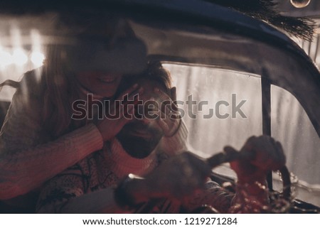 Young man with beard and his girlfriend in vintage car with pine tree celebrating Christmas