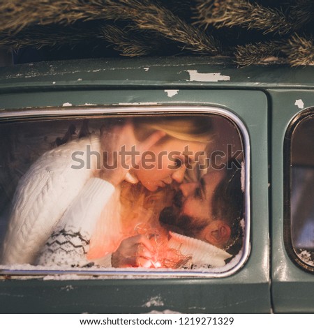 Young man with beard and his girlfriend in vintage car with pine tree celebrating Christmas