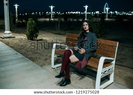 Young beautiful girl in a gray coat, in a gray skirt and burgundy stockings, photographs with a vintage camera