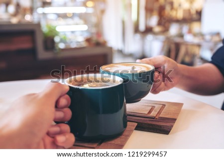 Close up image of a man and a woman clinking green coffee mugs in cafe