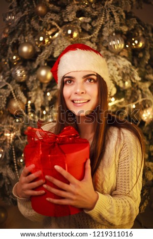 Happy dreamy young woman with a gift at home on the background of the New Year tree and decorations