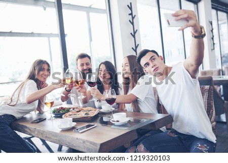 A group of people make a selfie photo in a cafe. The best friends gathered together at a dinner table eating pizza and singing various drinks.
