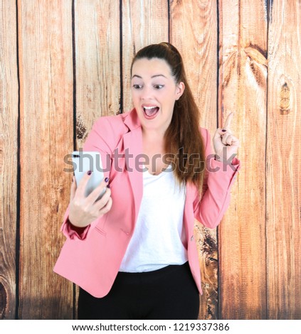 Excited business woman taking a picture with her phone while pointing her finger up against a wooden background