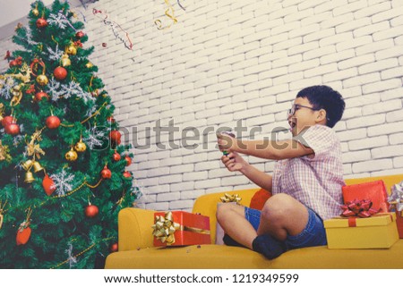 Christmas Celebration Concept : Asian boy wearing glasses, naive, happy, cheerful, playful, with a play Rainbow Popper on Christmas Eve

