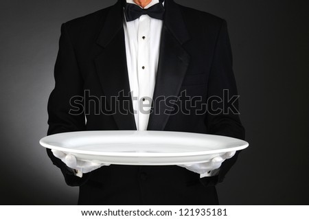 Waiter holding a large white platter over a light to dark gray background. Horizontal format, man is unrecognizable. Royalty-Free Stock Photo #121935181