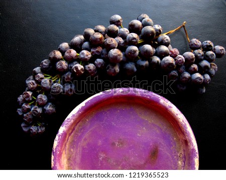 Bunch of grapes and a little dark purple dish on a black background. Still life