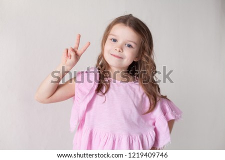 a little girl in a pink dress shows two fingers